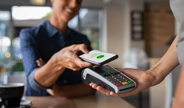 Mature woman paying bill through smartphone using NFC technology in a restaurant. Satisfied customer paying through mobile phone using contactless technology. Close up hands of mobile payment at a coffee shop.