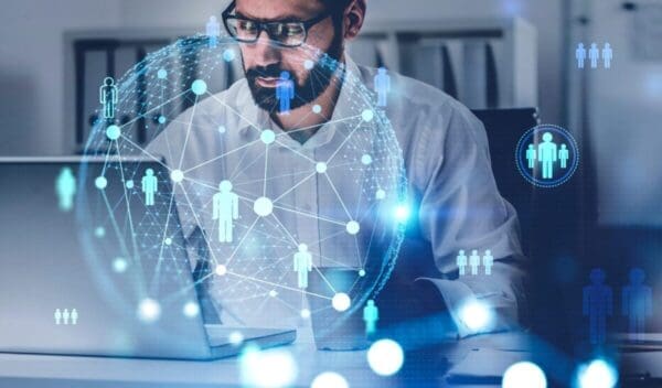 Young bearded businessman using laptop in blurry office with double exposure of social network interface. Concept of HR. Toned image