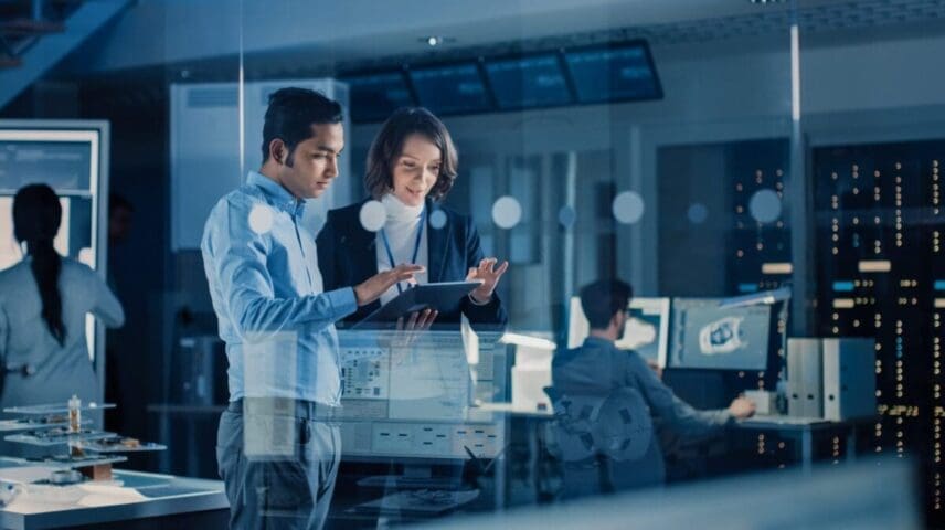 In Technology Research Facility: Female Project Manager Talks With Chief Engineer, they Consult Tablet Computer. Team of Industrial Engineers, Developers Work on Engine Design Using Computers