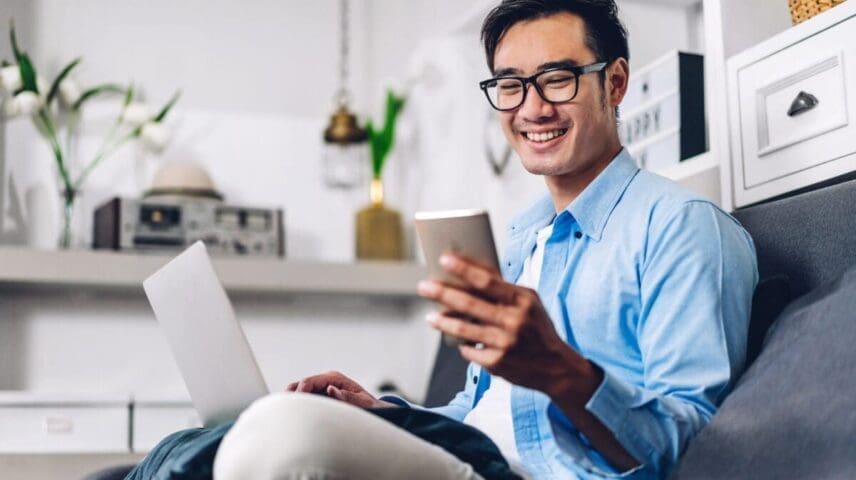 Young smiling asian man relaxing using laptop computer working and video conference meeting at home.Young creative man looking at screen typing message with smartphone.work from home concept