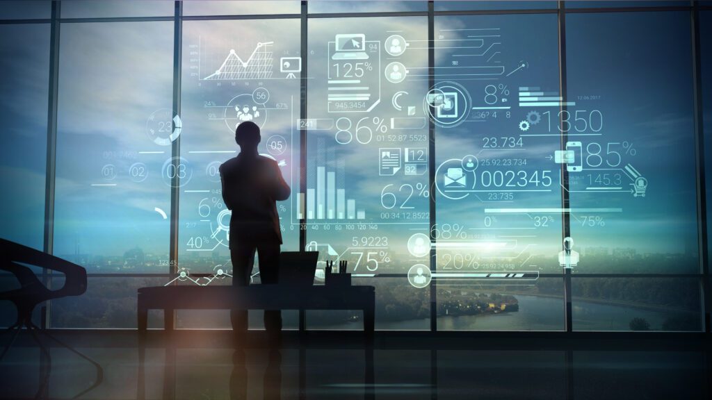 A silhouette of a man stands on the background of large office windows and views a hologram of corporate infographic with work data.